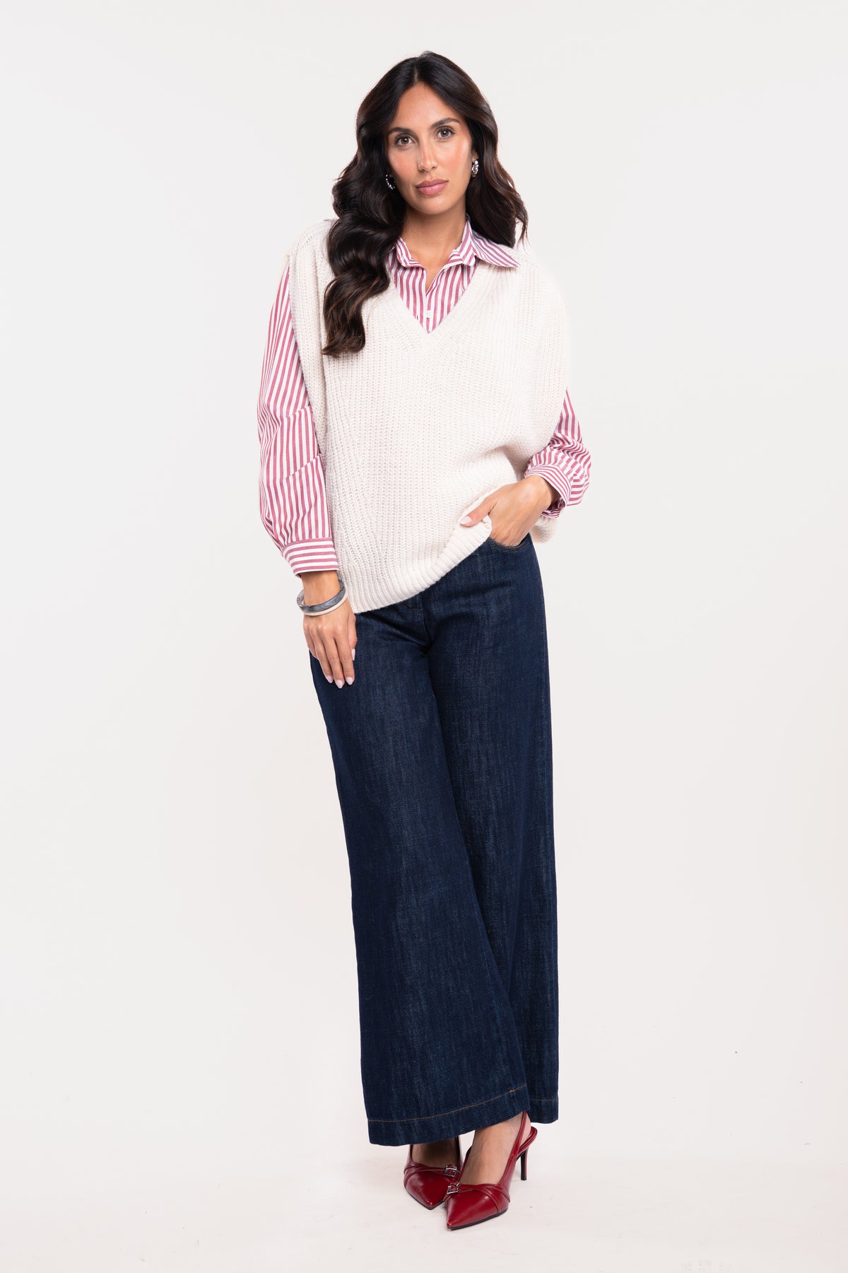 Pull ample col V écru, chemise à rayures rouge, pantalon en jean brut et paire de talons rouges