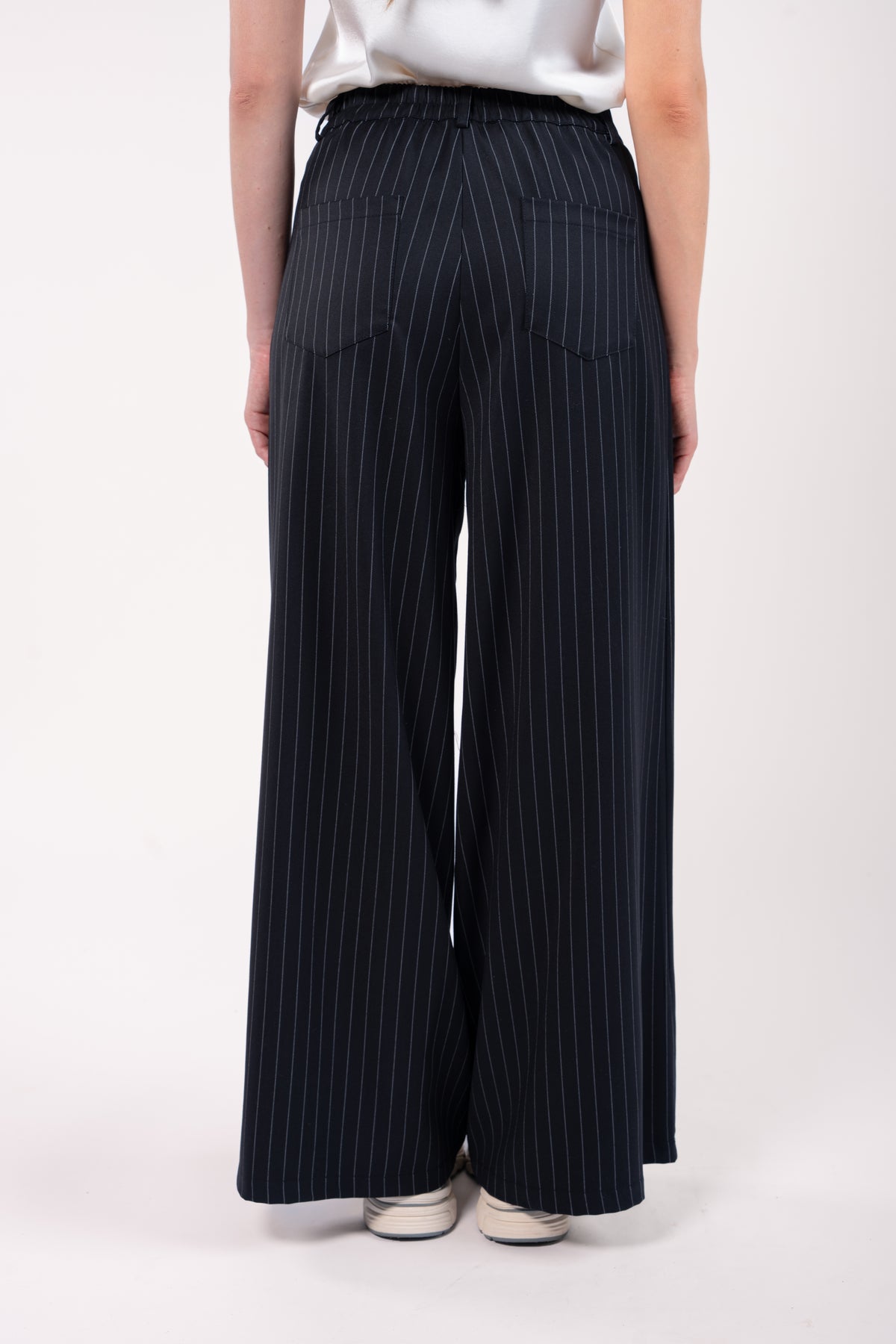 Pantalon maxi évasé rayé noir avec t-shirt naturel et basket blanche de dos