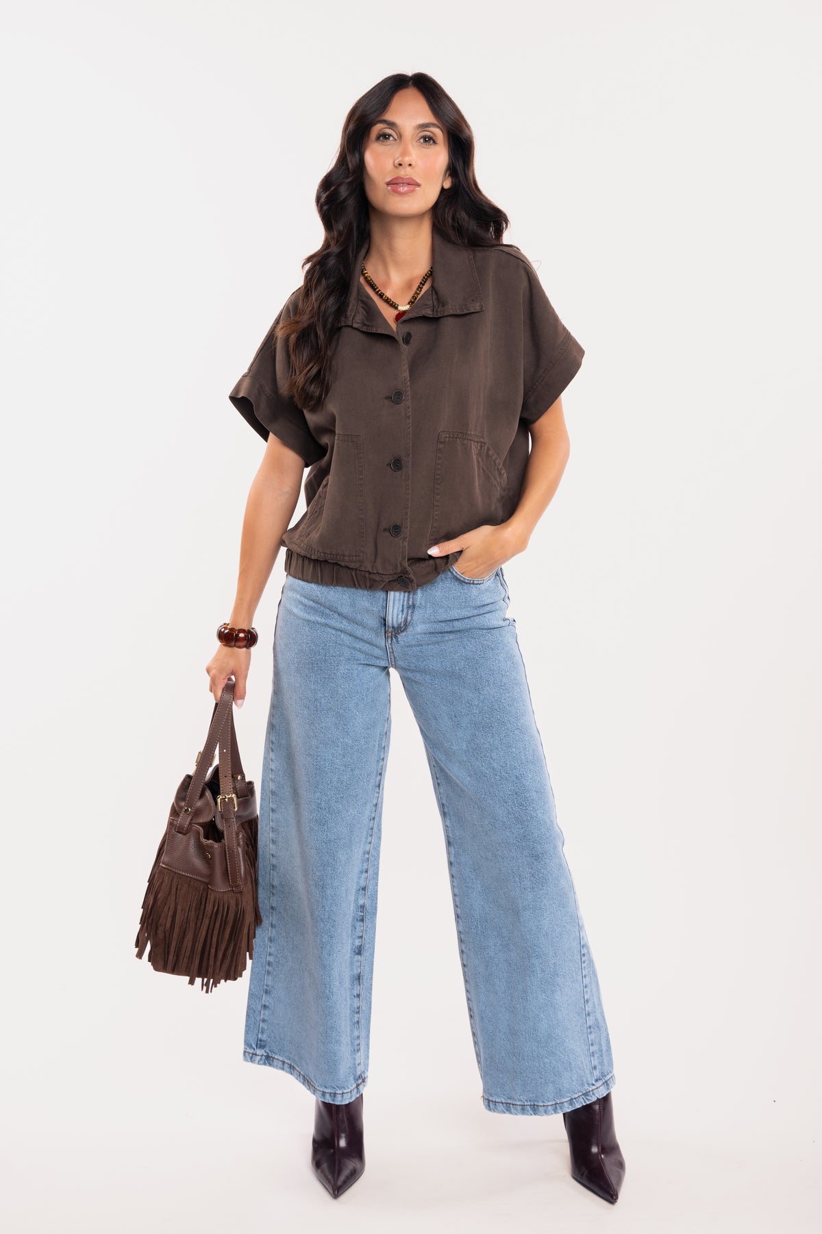 Une veste sans manches marron, un jean évasé délavé clair, une paire de talons et un sac en cuir marron à franges