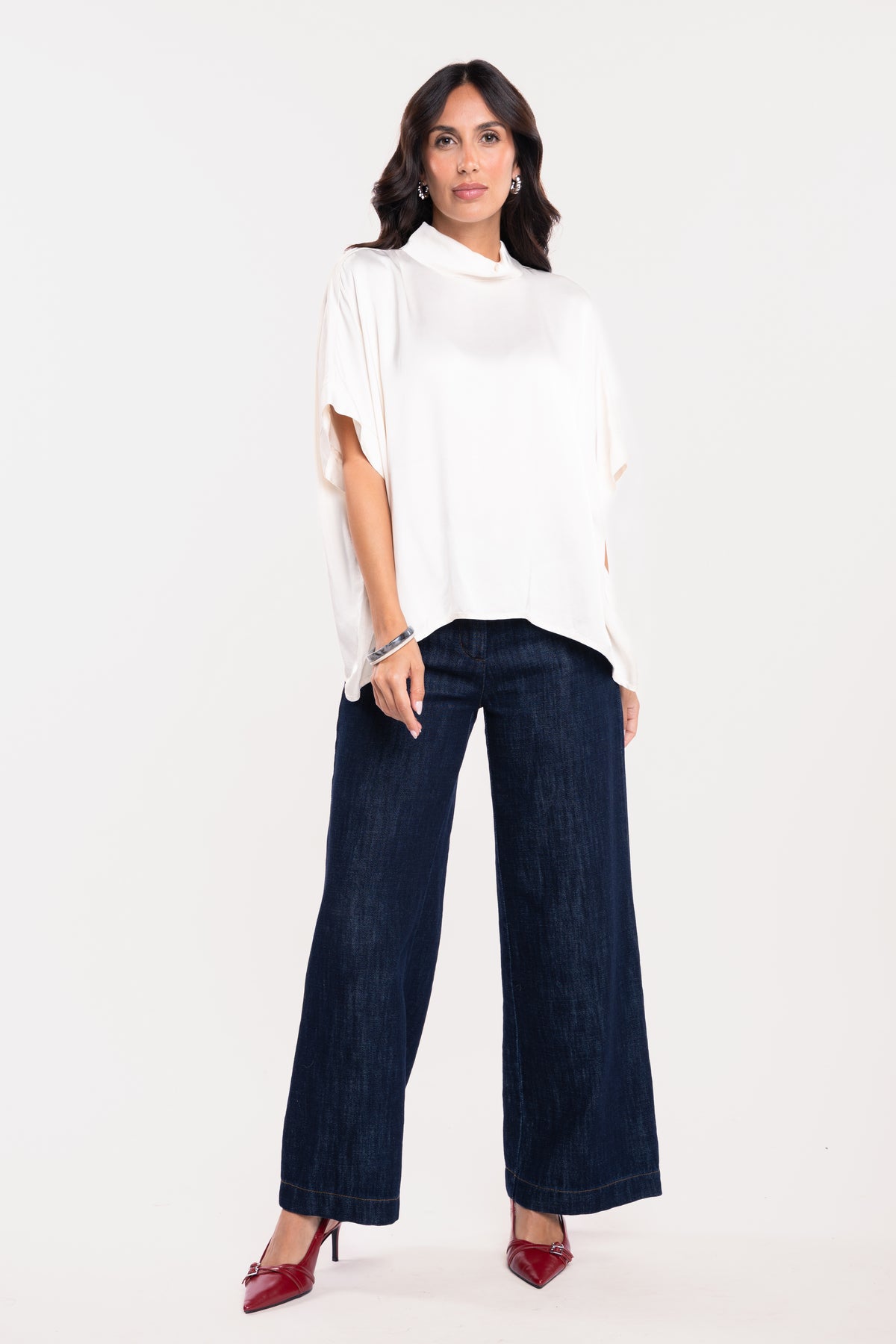 Une blouse à col montant écrue, un pantalon en jean brut et une paire de talons rouges