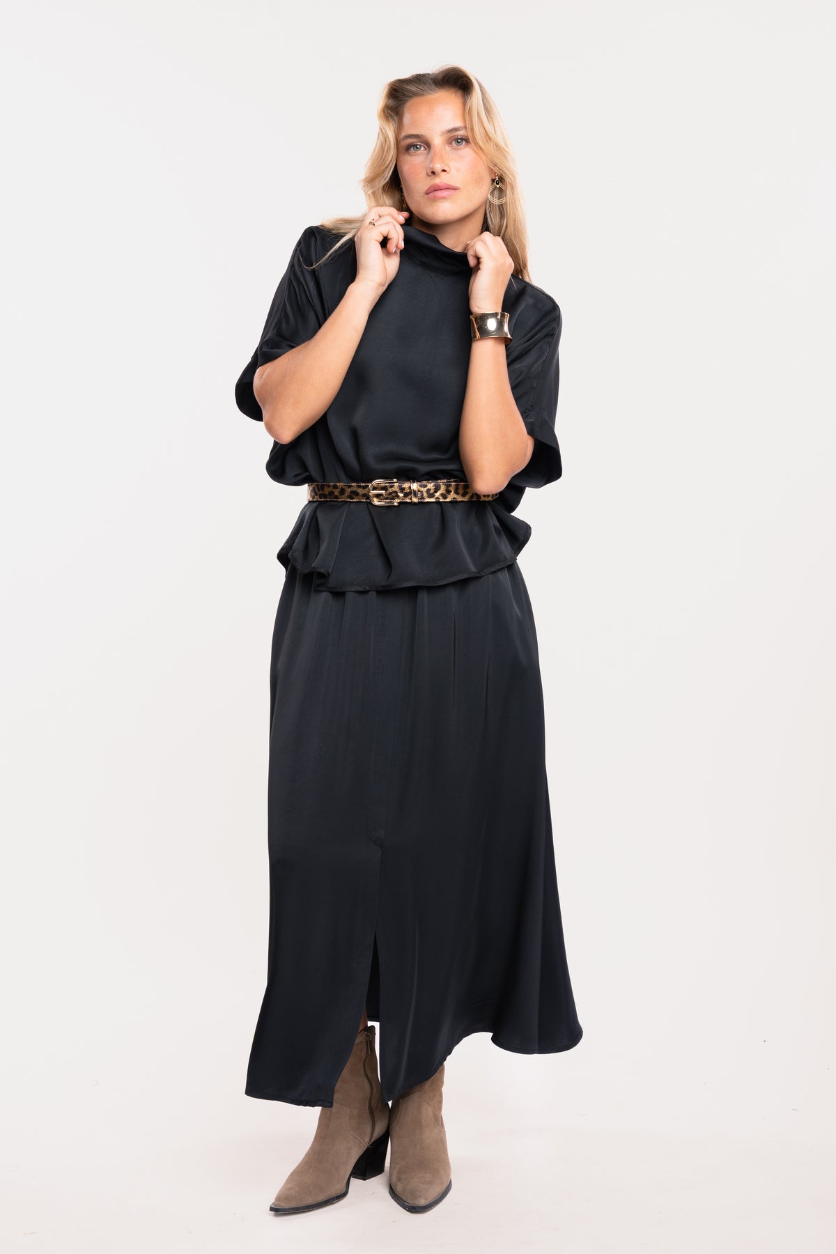 Une blouse noire à col montant, une ceinture imprimée léopard, une jupe mi-longue fendue sur le devant et paire de talons beiges 