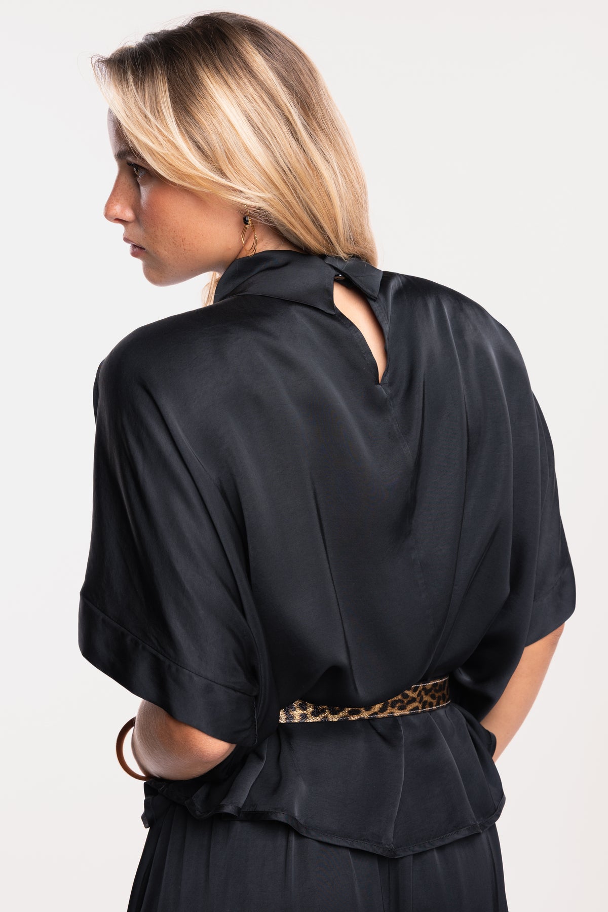Une blouse noire à col montant, une ceinture imprimée léopard et une jupe mi-longue fendue sur le devant de dos