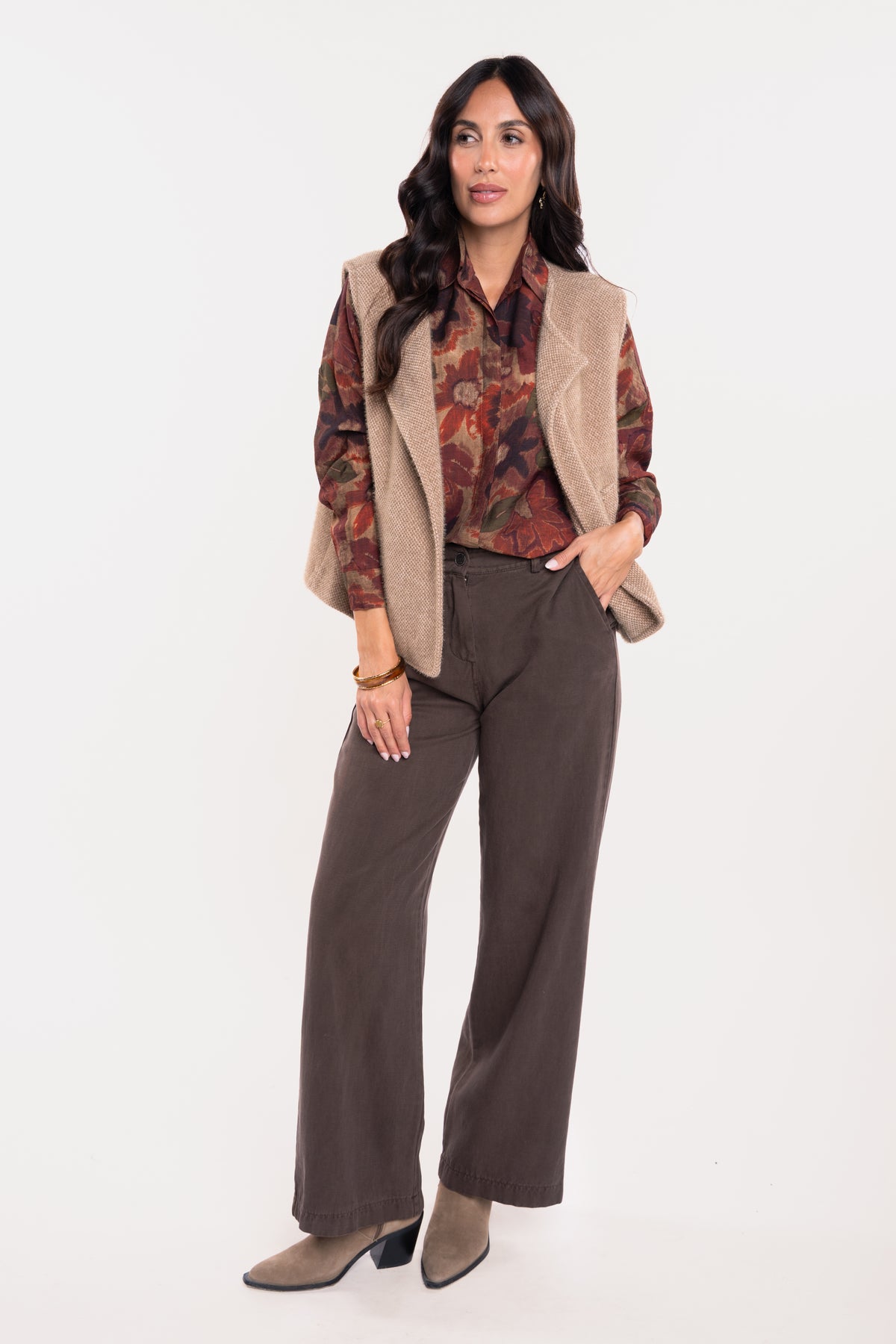 Gilet sans manches camel avec chemise imprimée fleuris prune, pantalon évasé marron et paire de bottes beiges 
