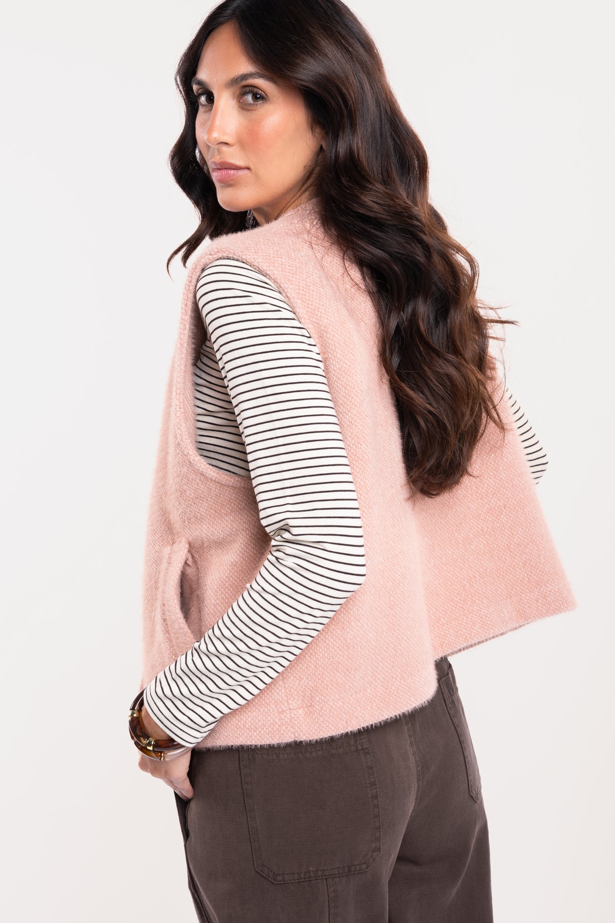 Gilet sans manches vieux rose avec t-shirt col v rayé écru et marron avec un pantalon barrel marron de dos