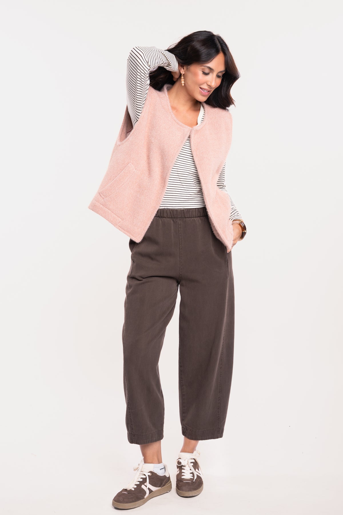  Gilet sans manches vieux rose avec un t-shirt col V rayé écru et marron, un pantalon barrel marron et une paire de baskets marron