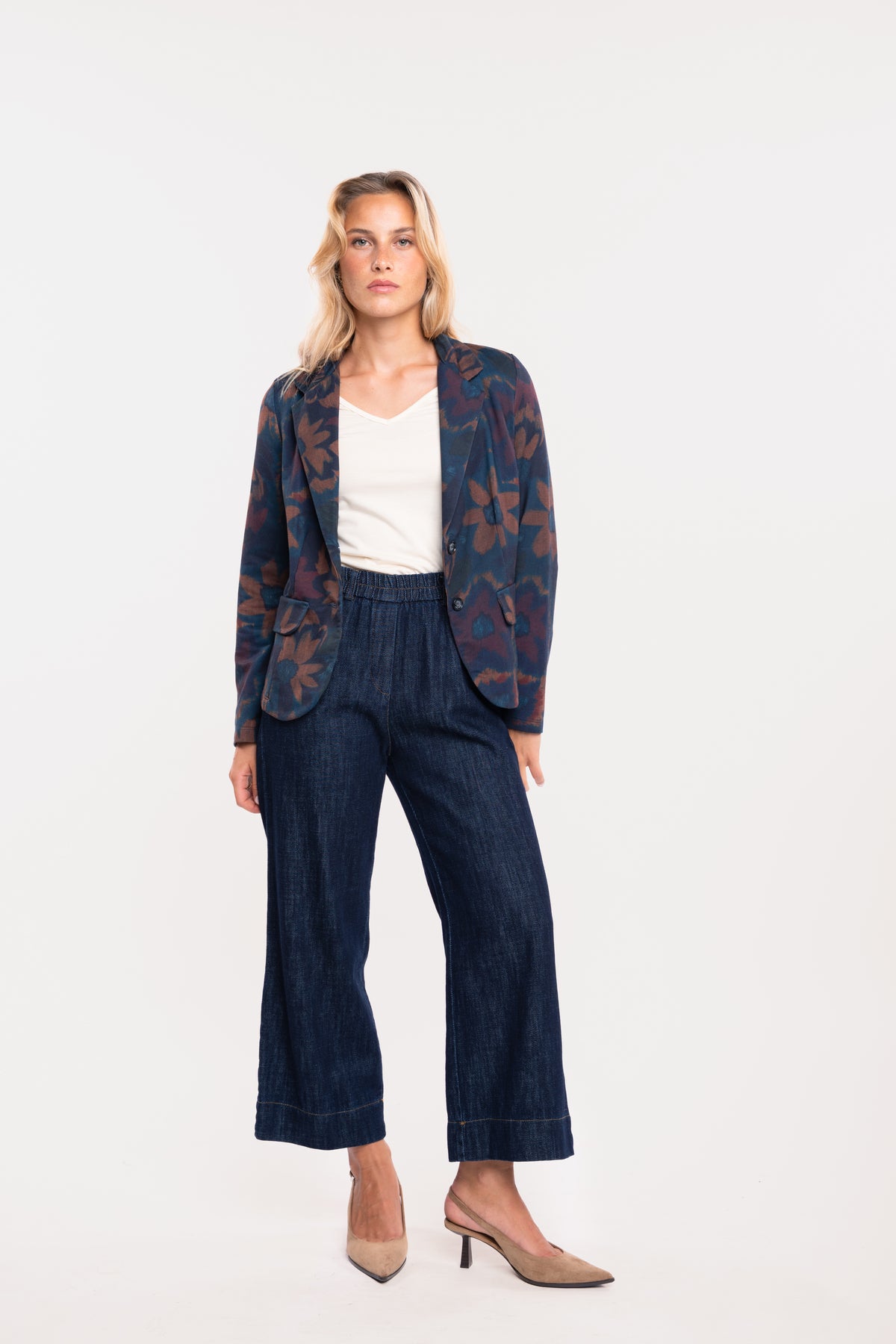 Un blazer imprimé fleuri bleu marine, un T-shirt à col V écru, un jean évasé brut et une paire de talons beiges 