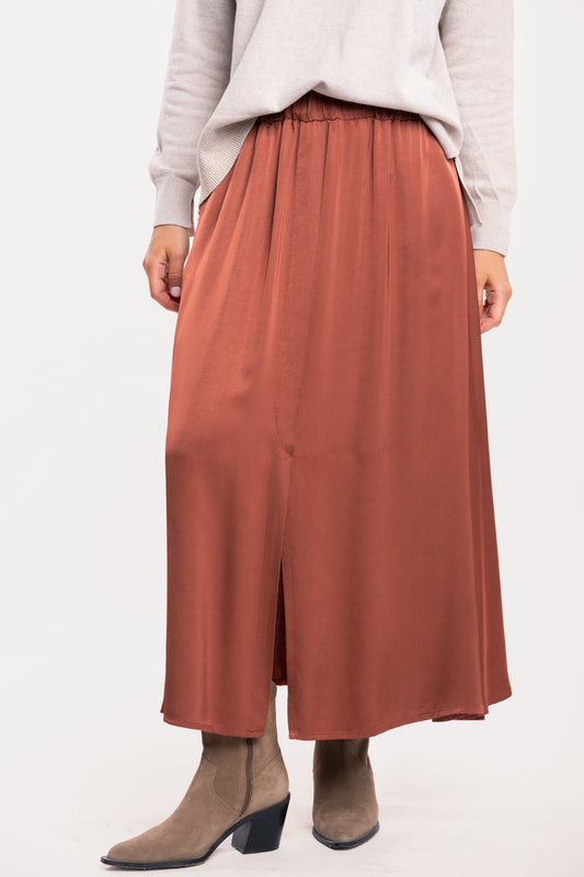 Un pull oversize beige, une jupe midi fluide acajou et une paire de bottes beiges