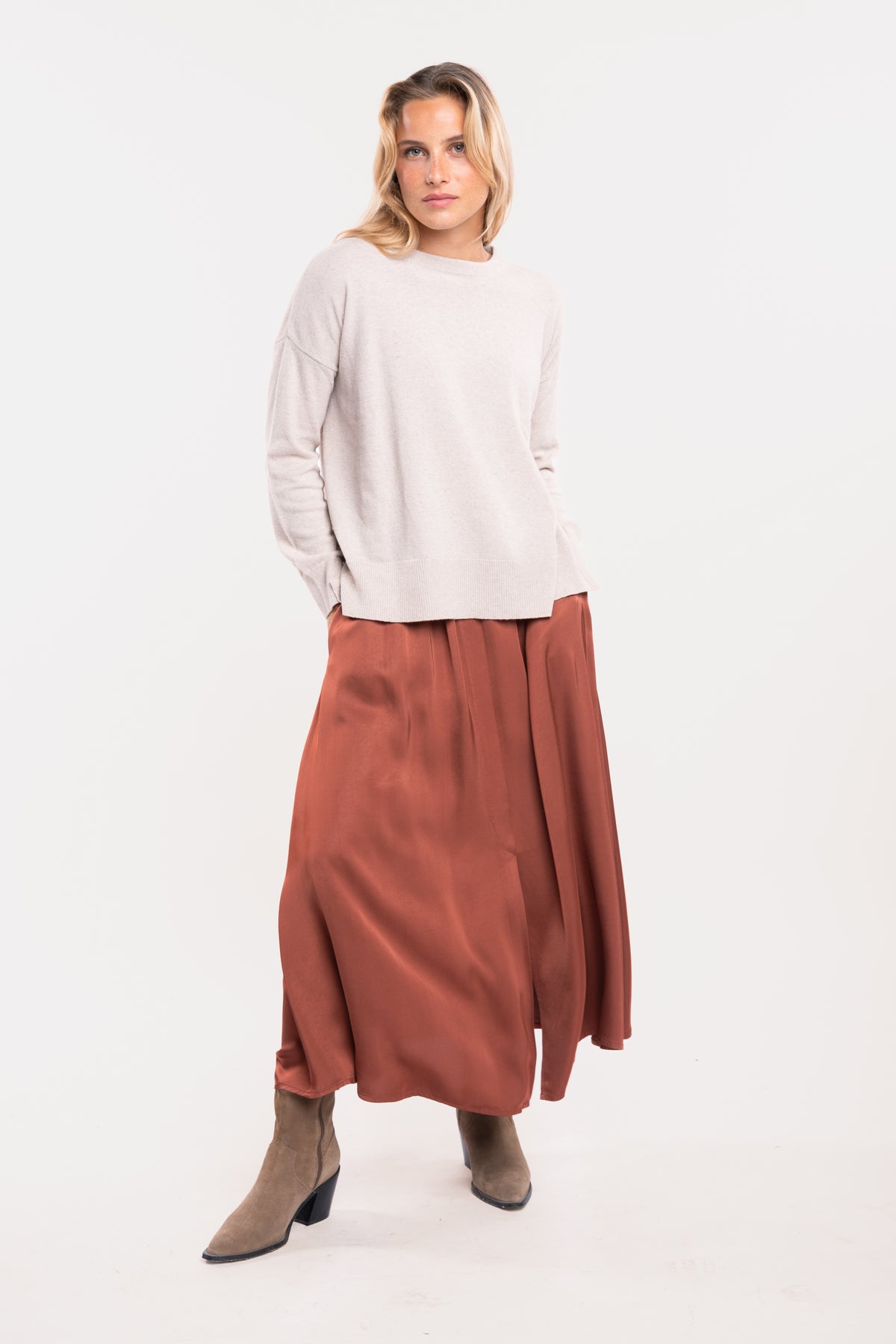 Un pull oversize beige, une jupe midi fluide acajou et une paire de bottes beiges