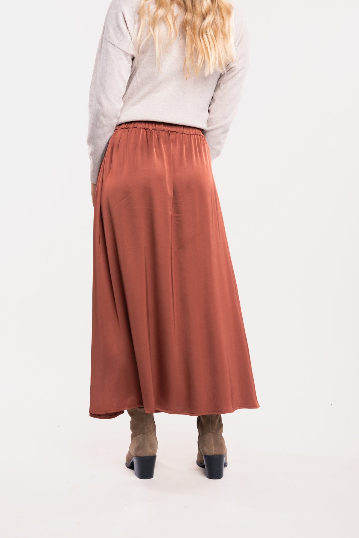 Un pull oversize beige, une jupe midi fluide acajou et une paire de bottes beiges de dos