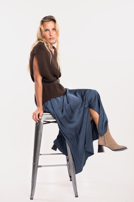 Un pull ample à col V marron, une ceinture en daim marron, une jupe midi fluide bleu nuit et une paire de bottes beiges 