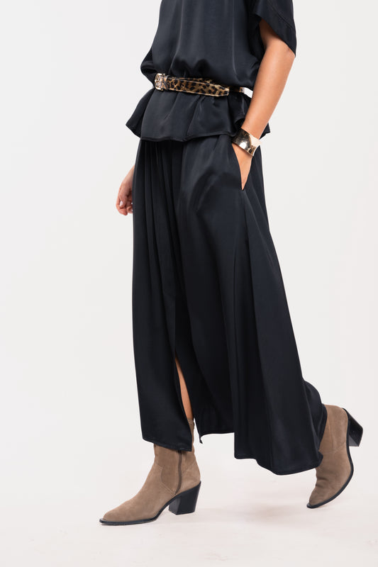 Une blouse à col chemine noire, une ceinture en cuir léopard, une jupe midi fluide noire et une paire de bottes beiges