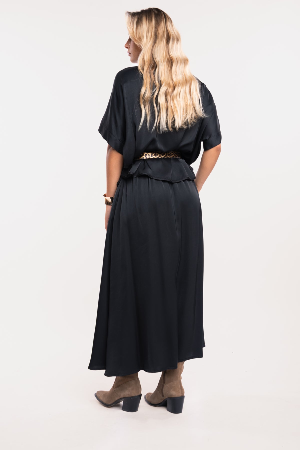 Une blouse à col chemine noire, une ceinture en cuir léopard, une jupe midi fluide noire et une paire de bottes beiges de dos