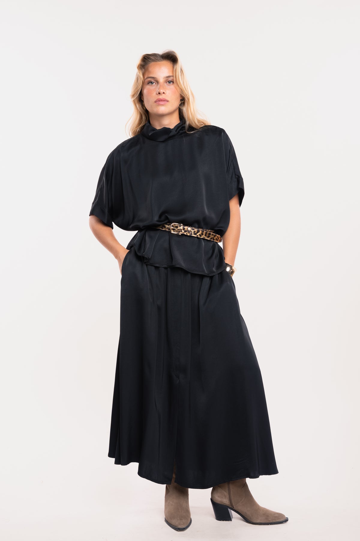Une blouse à col chemine noire, une ceinture en cuir léopard, une jupe midi fluide noire et une paire de bottes beiges