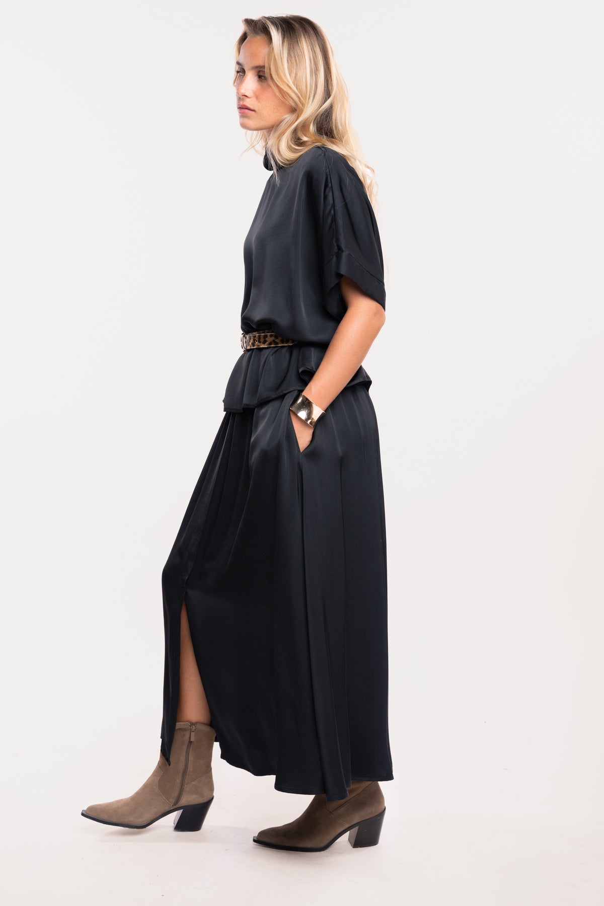 Une blouse à col chemine noire, une ceinture en cuir léopard, une jupe midi fluide noire et une paire de bottes beiges