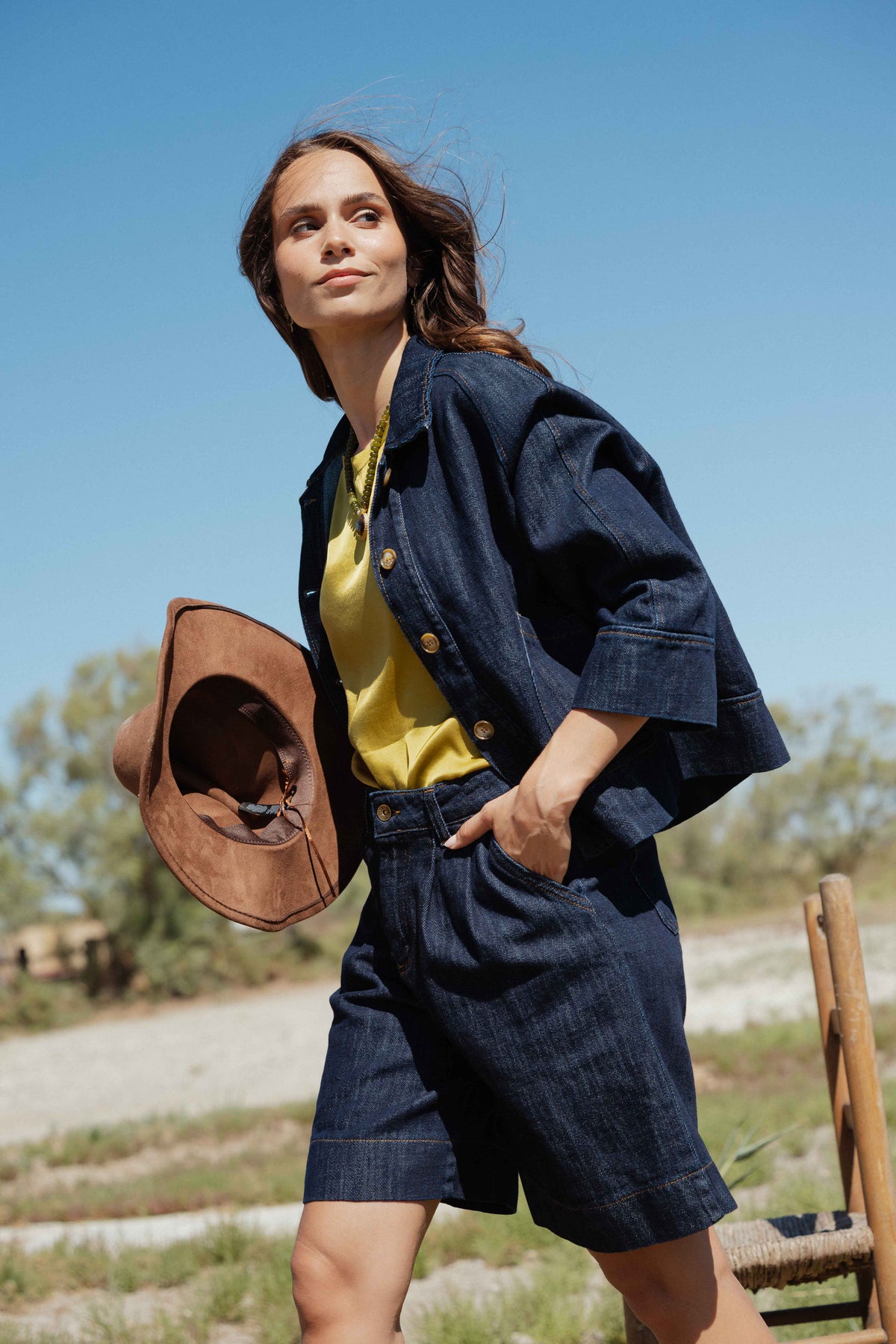 Veste en jean brut avec top satiné vert olive, bermuda en denim brut et chapeau marron