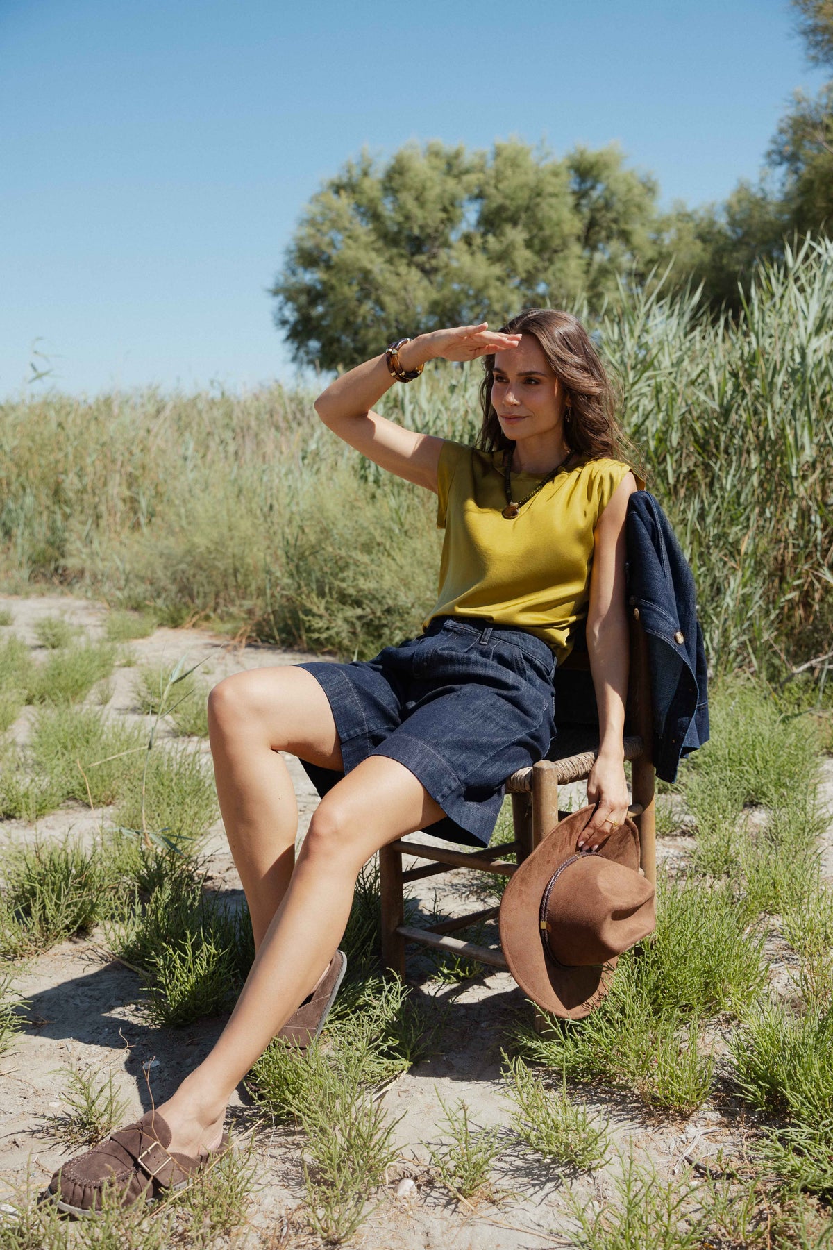 Top satiné vert olive, bermuda en denim brut, veste en jean brut et chapeau marron