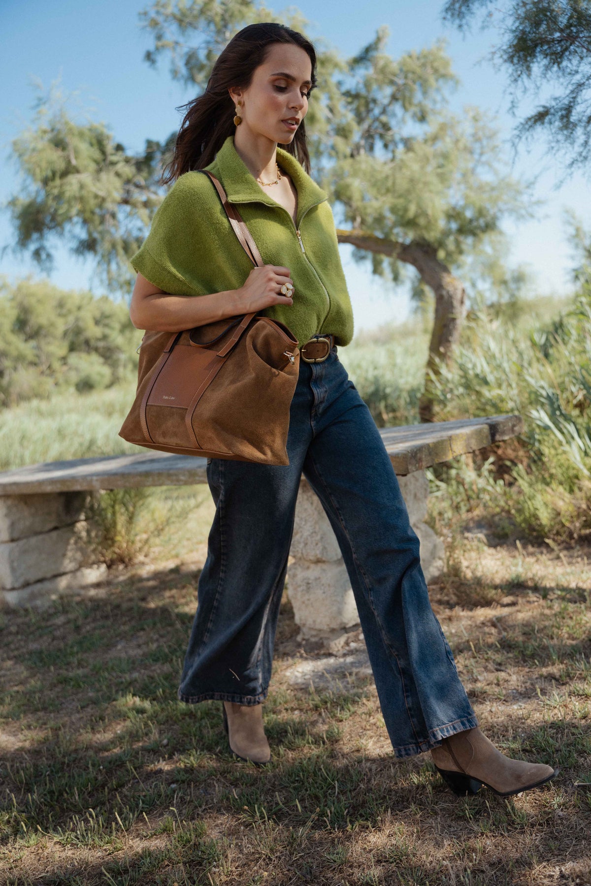 Veste zipée oversize vert olive, ceinture en daim marron, jean évasé délavé, sac cabas en cuir camel et bottes beiges à talon  