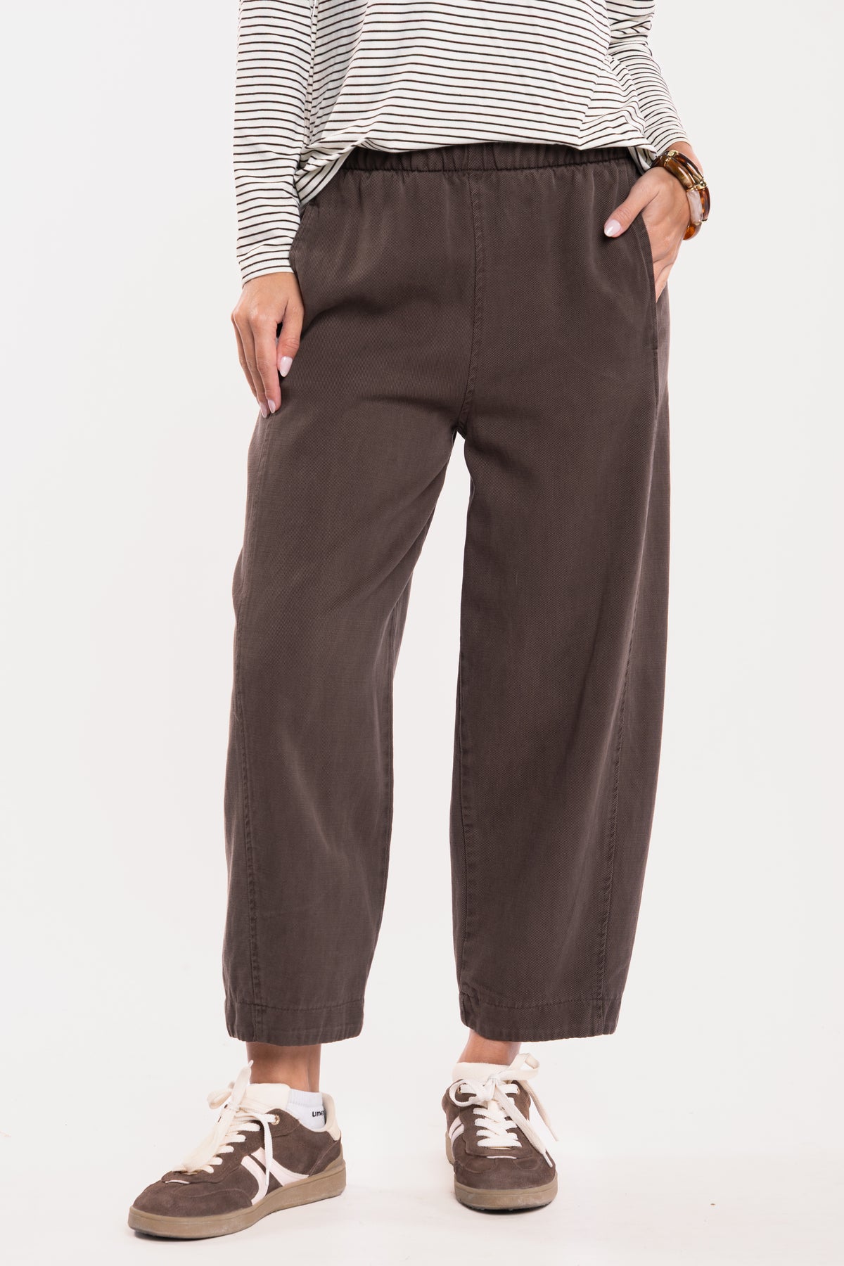 T-shirt col V rayé écru et marron, un pantalon ballon marron et une paire de baskets marron 