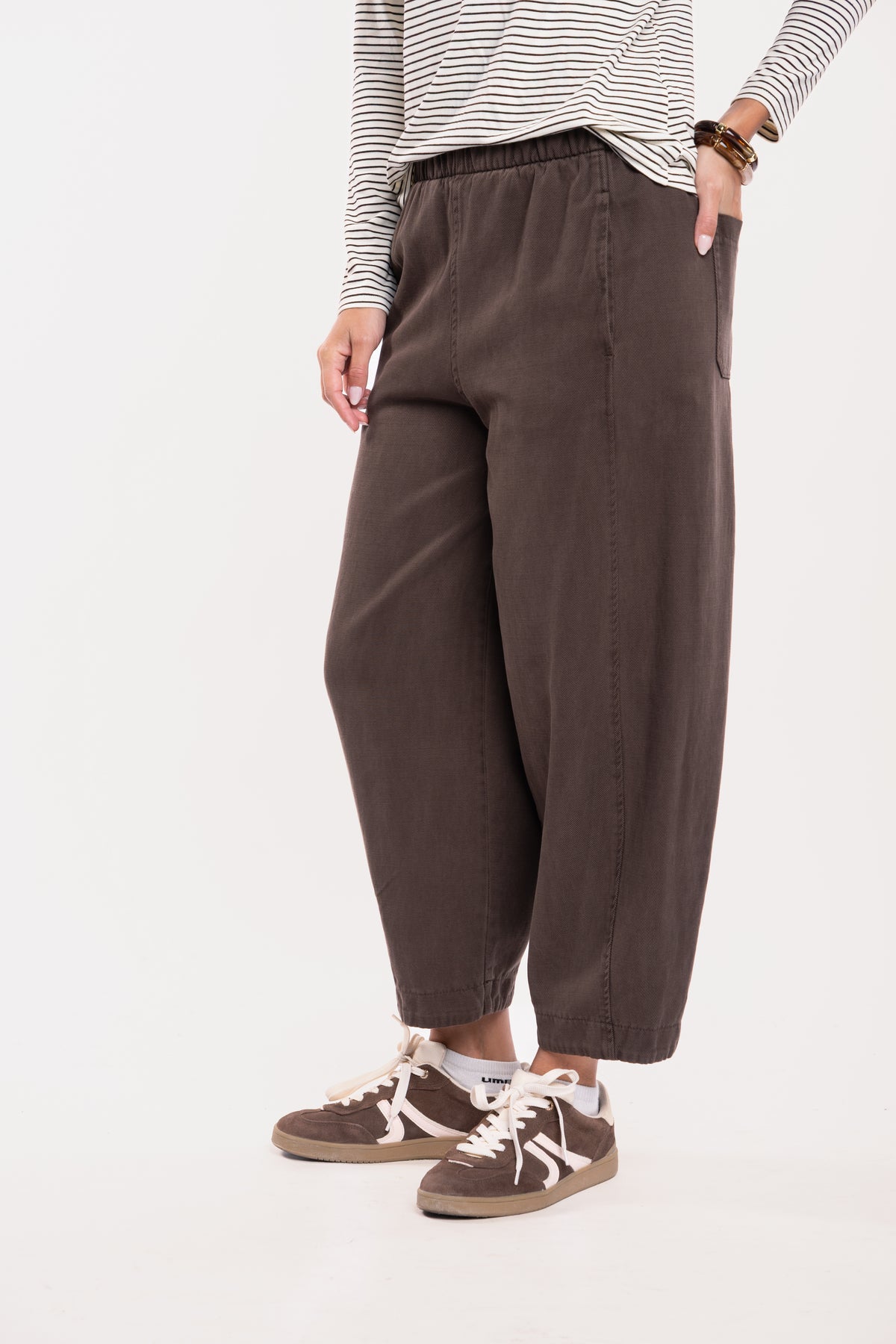  T-shirt col V rayé écru et marron, un pantalon ballon marron et une paire de baskets marron 