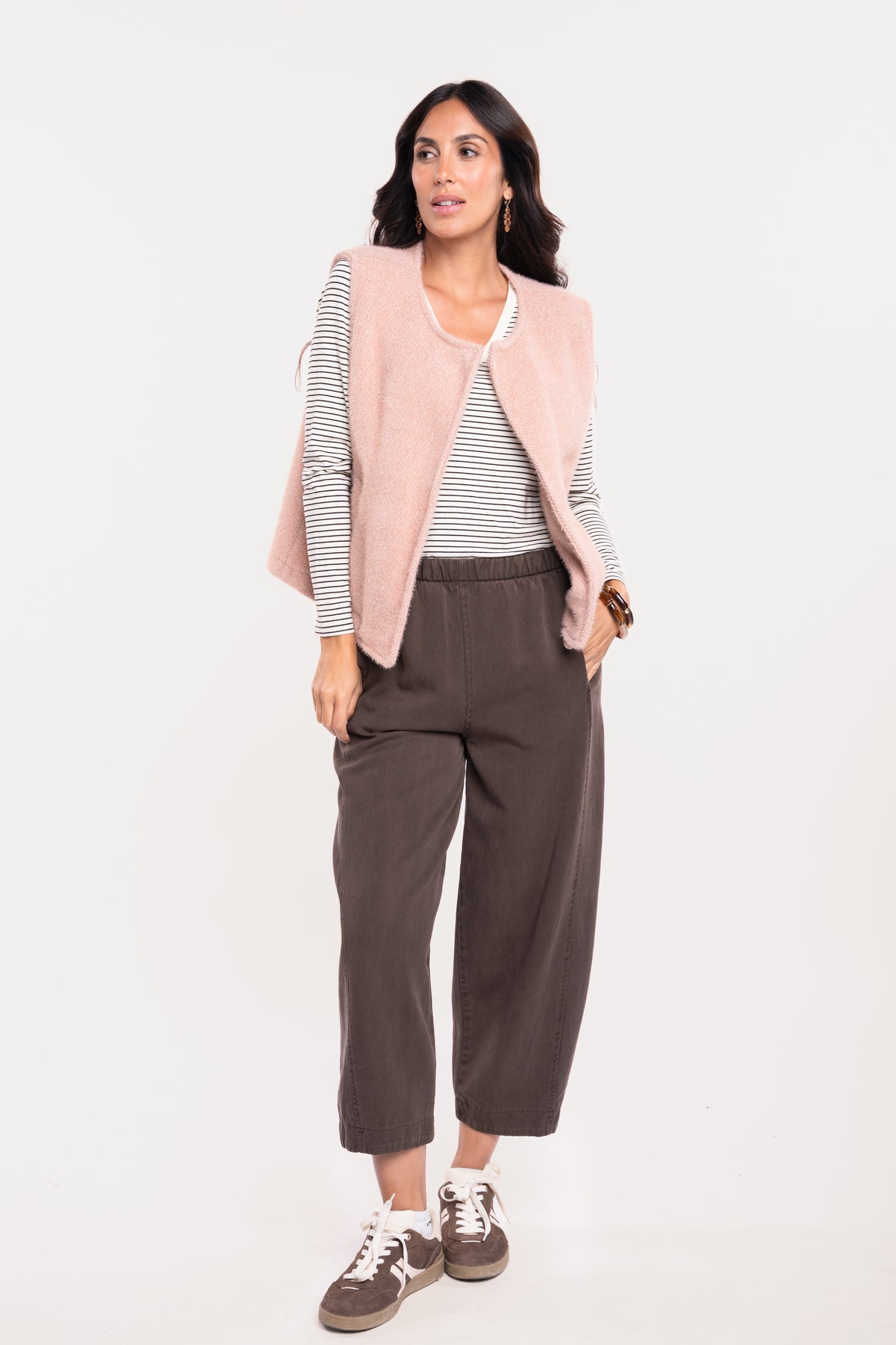 Gilet sans manches vieux rose avec un T-shirt col V rayé écru et marron, un pantalon ballon marron et une paire de baskets marron 