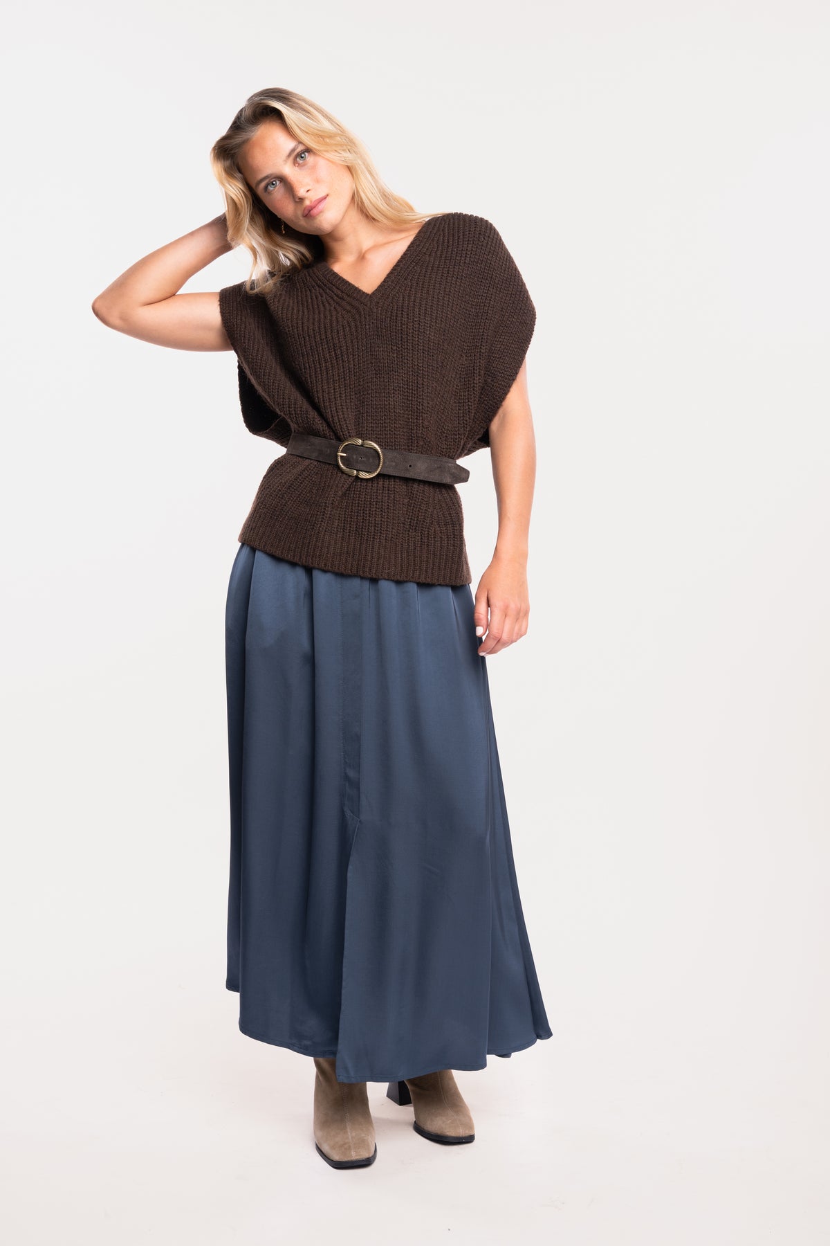 Un pull ample à col V marron, une ceinture en daim marron, une jupe mi-longue fendue sur le devant et une paire de bottes beiges