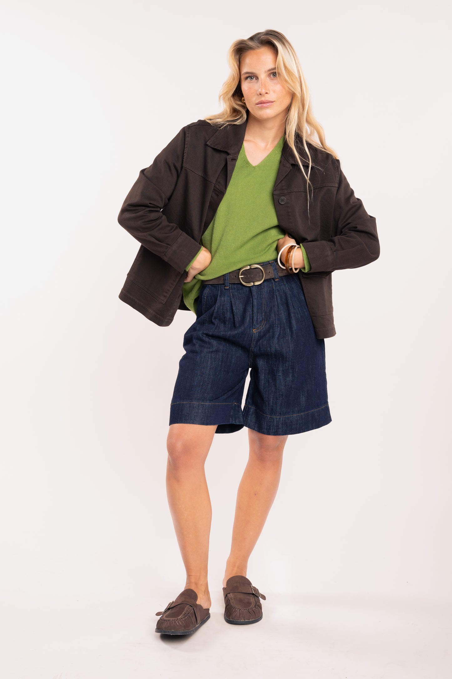 Pull ample femme vert, veste boutonnée marron, ceinture daim marron et bermuda long denim 