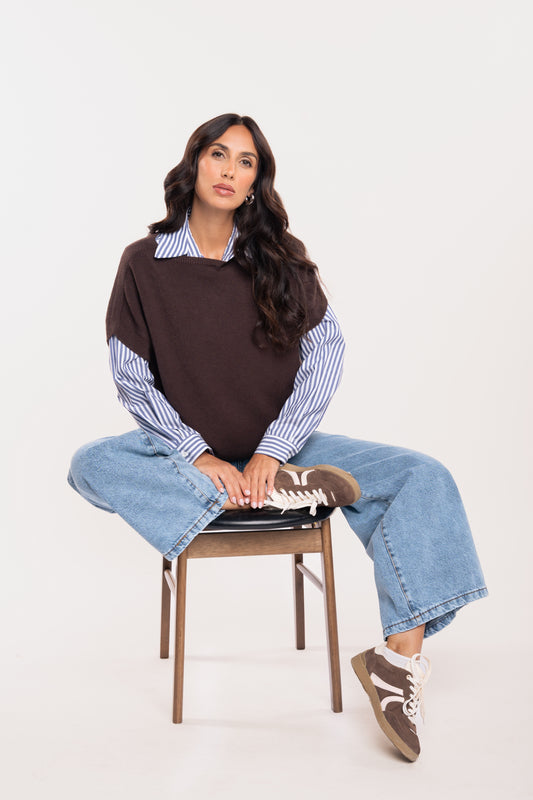 Pull sans manches marron avec une chemise rayée bleu marine, un jean évasé délavé clair et une paire de baskets marron 