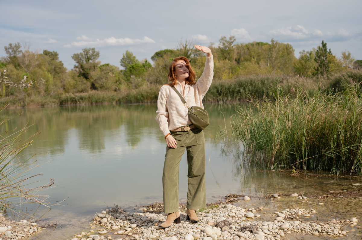 Pull écru, pantalon long en velours kaki, ceinture écru, sac en banane en cuir kaki et paire de bottes marron 