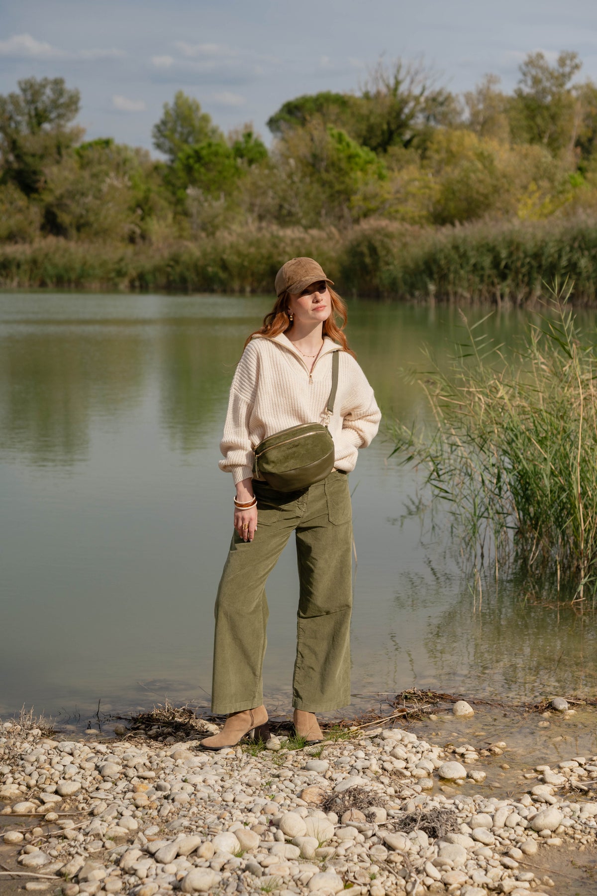 Pull écru, pantalon long en velours kaki, sac en banane en cuir kaki et paire de bottes marron 
