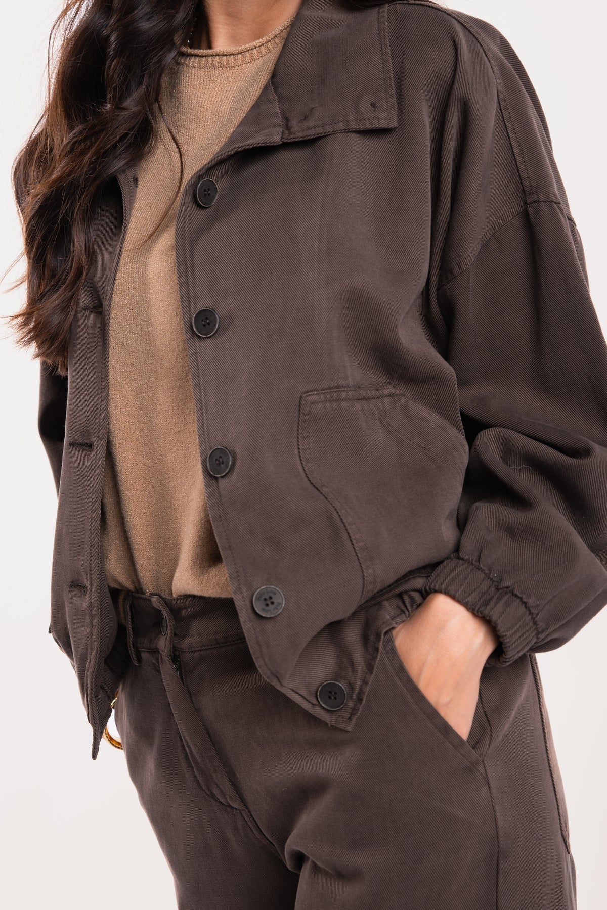 Une veste ample marron, un pull à manches courtes camel, un pantalon évasé marron 