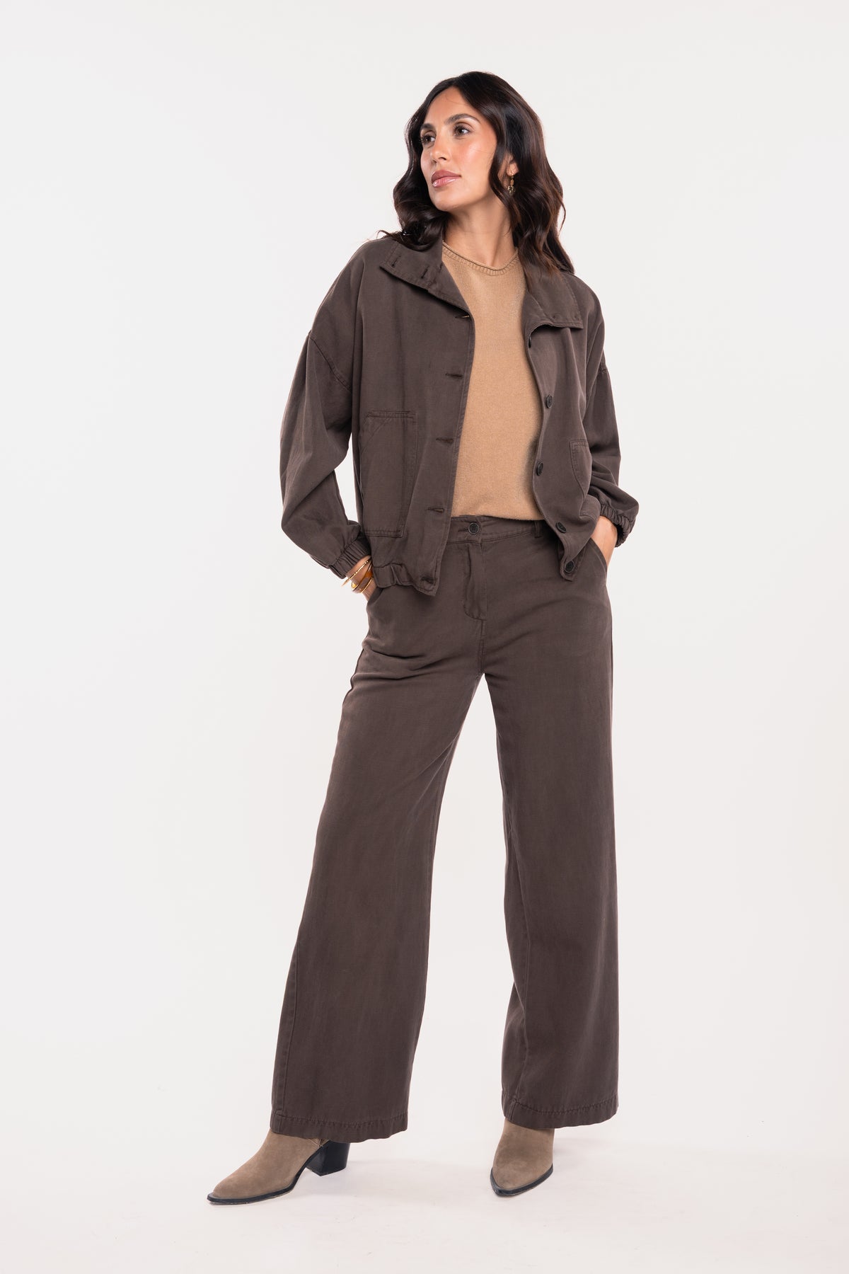 Une veste ample marron, un pull à manches courtes camel, un pantalon évasé marron et une paire de talons beiges 