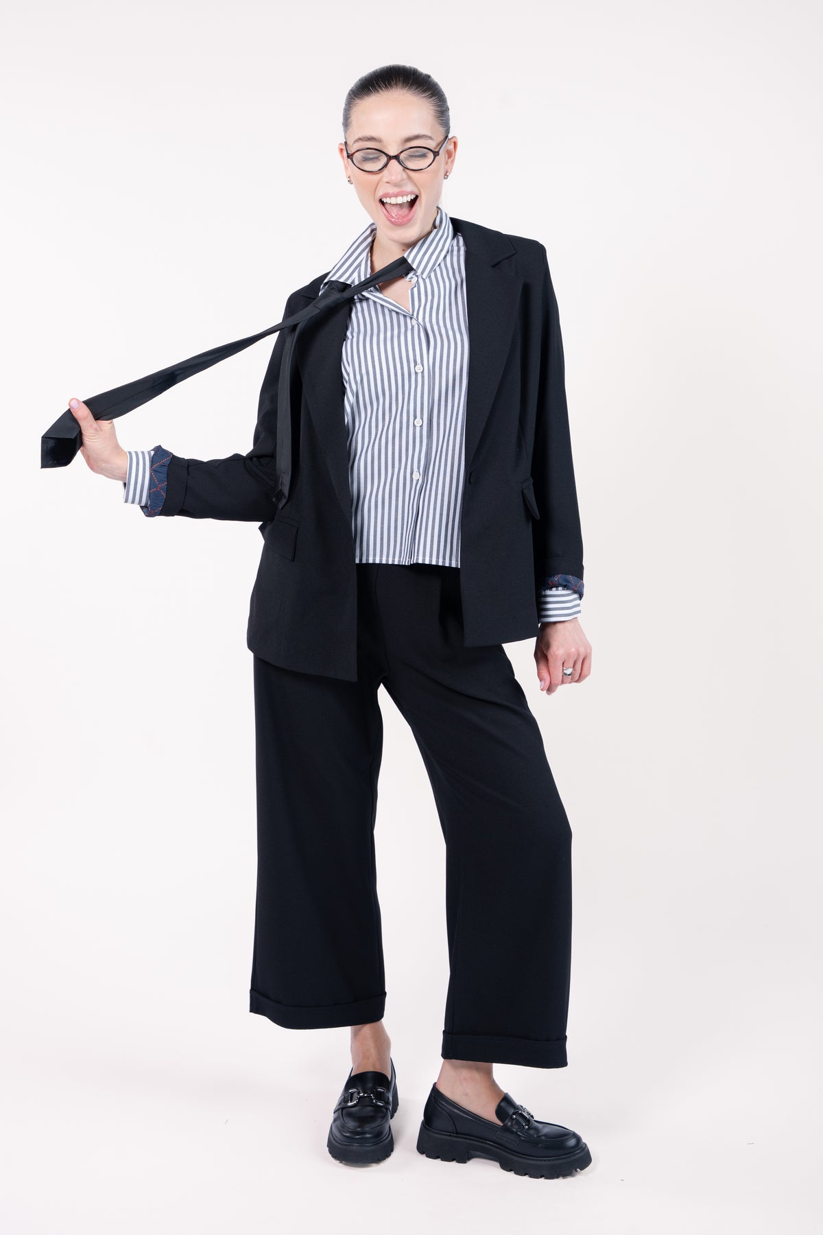 Blazer ample doublure PL noir, chemise courte manches longues rayées marine avec cravate noir, pantalon maxi évasé noir et mocassin noir 