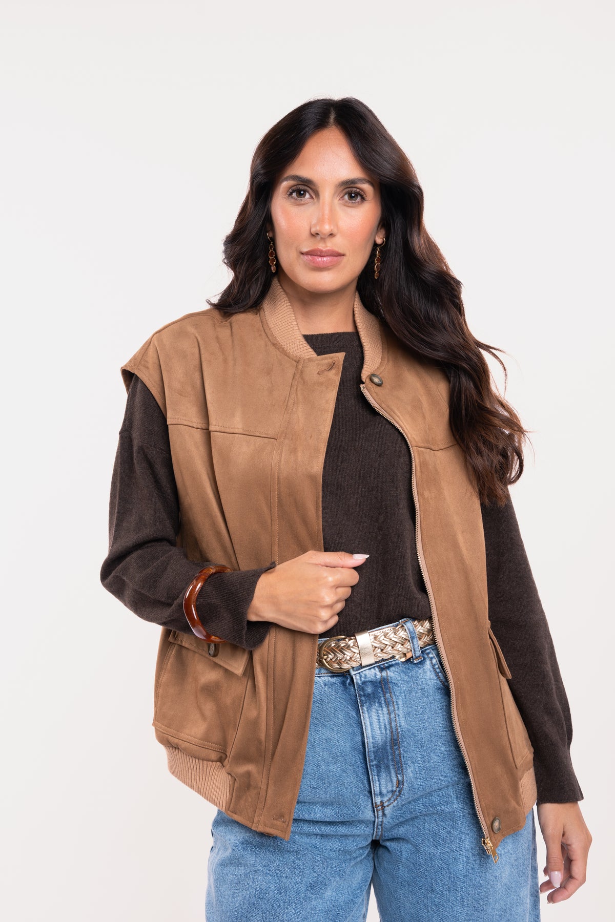 Veste sans manches suédine camel avec un pull oversize marron, une ceinture tressée en cuir doré et un jean barrel délavé clair 