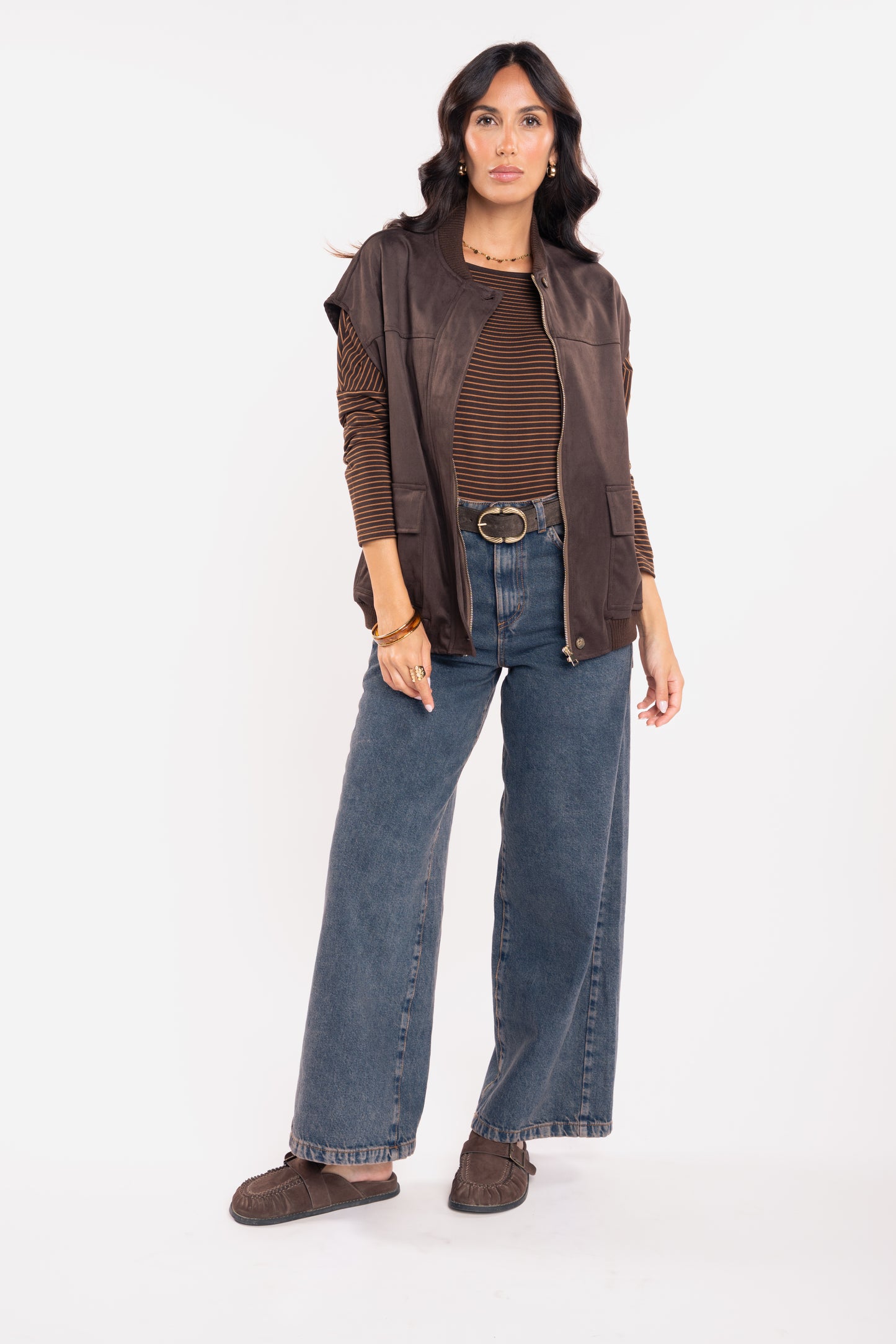 Veste sans manche suédine marron, top col bateau rayé marron, ceinture daim marron et jean évasé délavé 