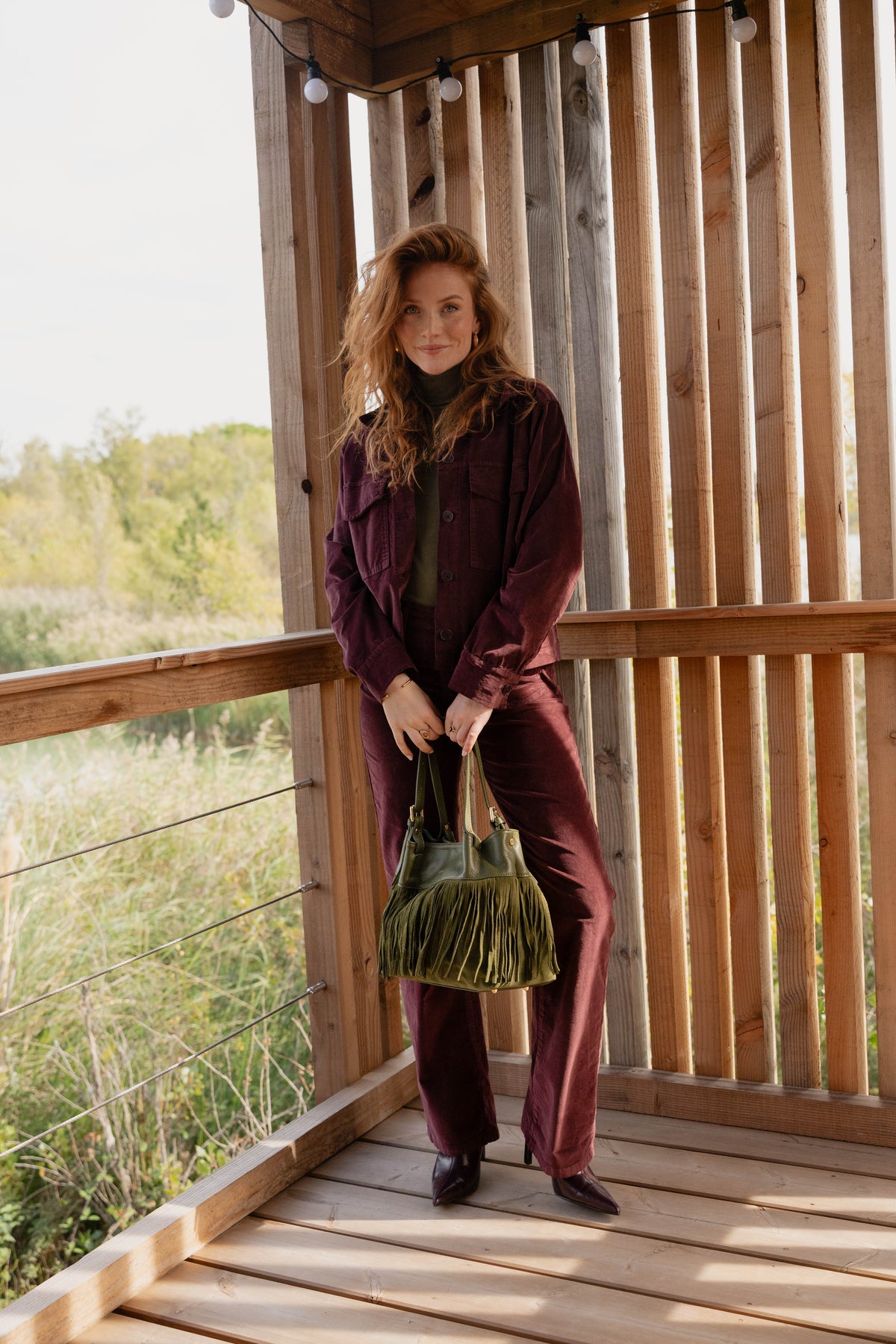 Veste en velours bordeaux avec un teeshirt col roulé kaki, un pantalon long en velours, un sac à frange kaki et une paire de chaussure bordeaux 